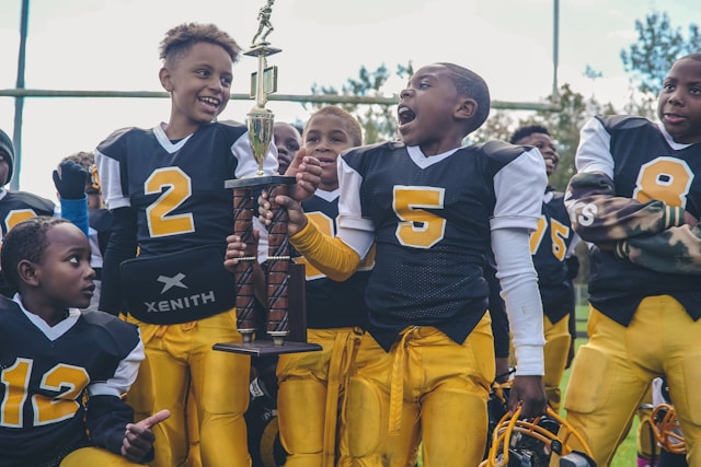 Black boys cheering a football win with trophy.